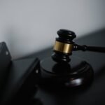 Black wooden gavel with golden strip on table near stack of folders in courthouse